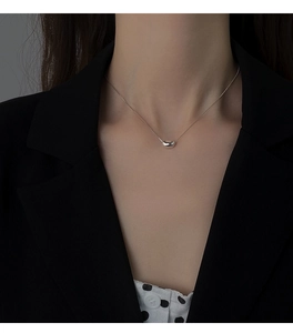 Close-up of minimalist silver bean pendant necklace worn by model on black blazer