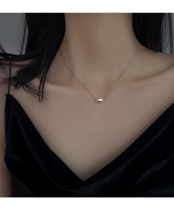 Macro detail of a minimalist silver bean pendant on an elegant necklace worn by a model