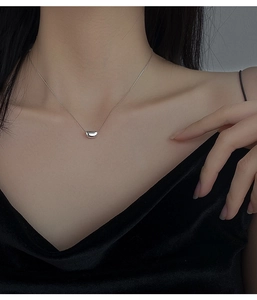 Close-up of minimalist bean pendant necklace in silver finish worn by a model