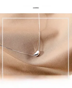 Detail view of a polished silver bean pendant on a delicate chain over satin fabric