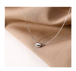 Macro shot of minimalist silver bean pendant on delicate box chain over silk fabric