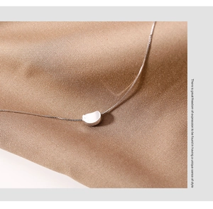 Macro shot of silver minimalist bean pendant on fine chain over silk fabric