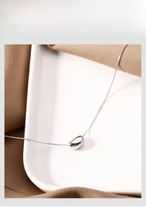 Detailed view of silver bean pendant on a fine box chain in a minimalist white tray