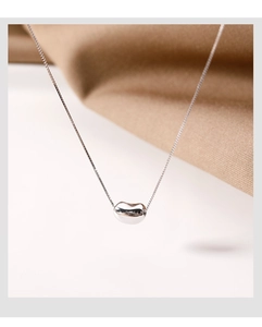 Macro shot of silver bean pendant on delicate chain with soft fabric background