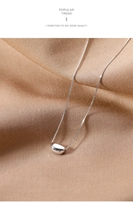 Macro detail of silver bean pendant on a delicate box chain over champagne silk fabric