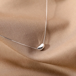 Minimalist silver bean pendant necklace on silk background for elegant women's jewelry style