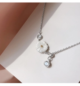 Close-up of silver chain necklace featuring a white shell daisy pendant and clear zircons