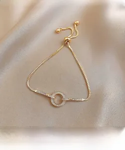 Detail van gouden verstelbare armband met ronde hanger bezet met zirkonia steentjes