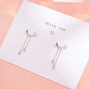 Boucles d'oreilles nœud papillon argentées avec pompons et zircons sur carte cadeau