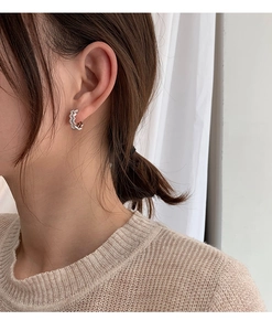 Close-up of minimalist silver wavy hoop earrings worn by a model in a knit sweater