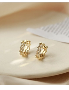 Detailed macro shot of wavy gold hoop earrings paved with sparkling zircon stones