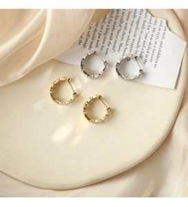 Macro detail of wave-shaped hoop earrings with sparkling white zircons in gold and silver