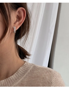 Detail of wavy silver earring with pavé-set clear zircons worn by a model
