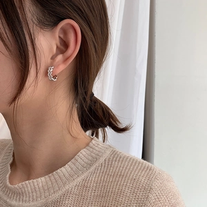 Silver wavy hoop earrings with zircon stones worn by a model in soft lighting
