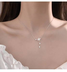 Nahaufnahme einer silbernen Kirschblütenkette mit rosa Zirkon-Anhängern auf dem Dekolleté