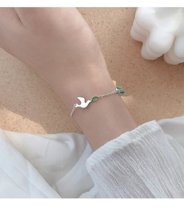 Détail d'un bracelet en argent s925 avec pendentif colombe et pierres vertes au poignet