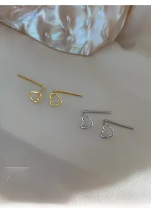 Close-up of minimalist gold and silver hollow heart earrings on a soft fabric background