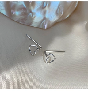 Detailed close-up of hollow heart-shaped silver earrings on soft white satin fabric