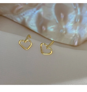 Detailed macro shot of golden hollow heart earrings on a silky fabric background