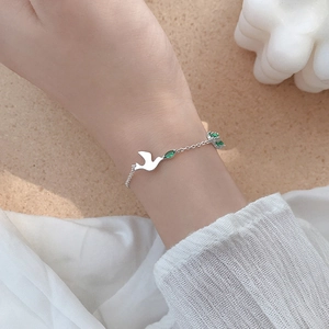 Bracelet hirondelle en argent S925 avec zircon vert au poignet sur fond de tissu élégant