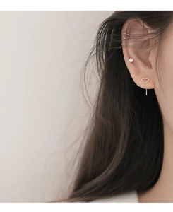 Close-up of minimalist silver hollow heart earrings and small zircon stud on woman's ear