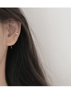 Close-up of minimalist hollow heart-shaped gold earrings and sparkling stud on a model
