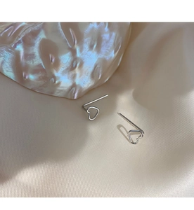 Close-up of minimalist silver heart drop earrings on soft beige velvet fabric background