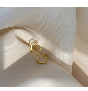Close-up of golden hollow heart earrings on elegant beige silk fabric texture