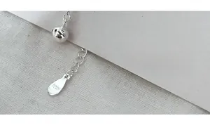 Dettaglio ravvicinato della catena di estensione in argento S925 con ciondolo lucido e campanello