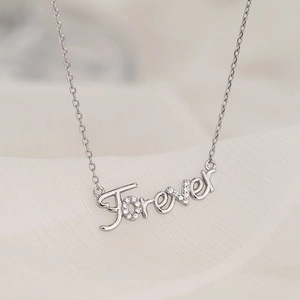 Silver Forever script necklace with micro-pave crystals on a white silk background