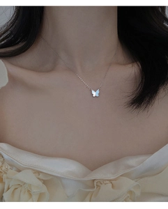 Gros plan d'un collier papillon en argent avec nacre bleue et blanche sur le cou