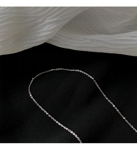 Gros plan d'un collier chaîne à billes argenté minimaliste sur un fond texturé noir et blanc