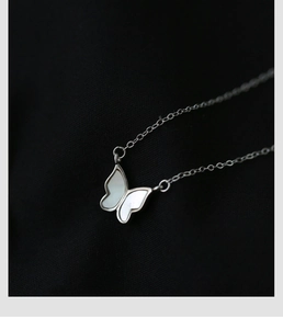 Gros plan du collier papillon en argent avec incrustation de nacre sur fond texturé