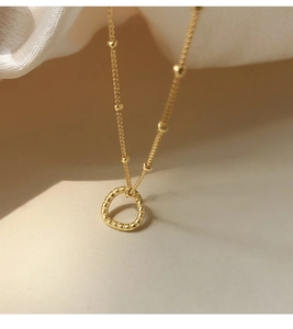 Macro shot of gold textured ring pendant on a beaded chain necklace with soft silk background