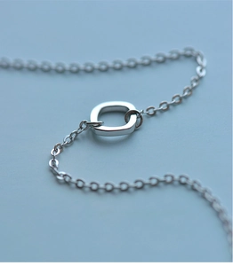 Macro shot of polished silver square charm and cross chain detail on a minimalist bracelet