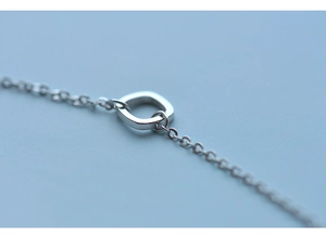 Detail shot of a minimalist silver square buckle and polished fine chain on blue background