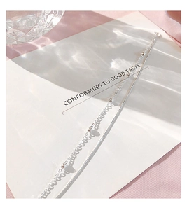Macro detail of a double-layer silver beaded chain bracelet on a soft pink satin background