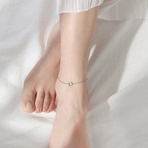 Minimalist square charm anklet in silver finish worn on ankle with white fabric background