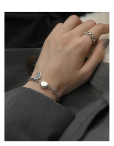 Detailansicht von Silberarmband mit Lucky-Anhänger und Ring auf grauem Stoffhintergrund