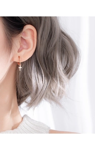 Detail of rose gold hoop earring with cross pendant worn on ear with soft lighting