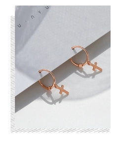 Detail of rose gold cross hoop earrings on white display card with sharp shadows