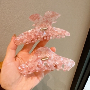 Detail showing two pink acetate hair claws with pearlescent plaid patterns and gold metal accents