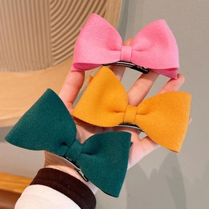Three wool bow hair clips in pink, yellow, and green held to show size and texture