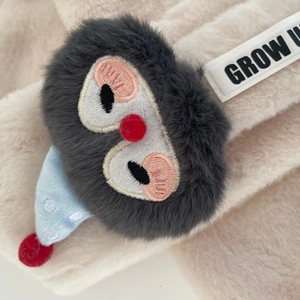Dettaglio di sciarpa in peluche per neonati con uccello grigio, cappello blu e etichetta Grow Up
