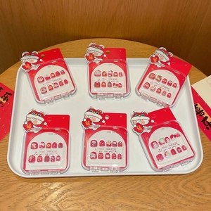 Detalle de uñas postizas rojas festivas pintadas a mano con motivos de lazos en estuches