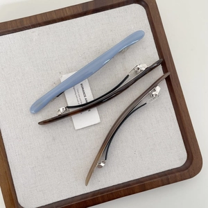 Dettaglio di fermagli per capelli in acetato blu, marrone e ambra su un vassoio di legno