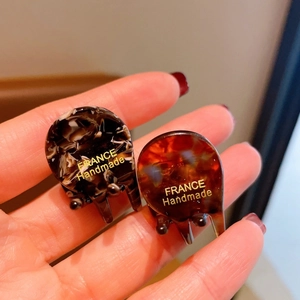 Detailed close-up of marble and amber acetate hair claws with gold handmade lettering