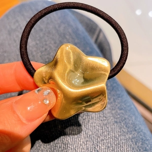 Dettaglio di un ciondolo a stella irregolare in oro opaco su un elastico per capelli nero
