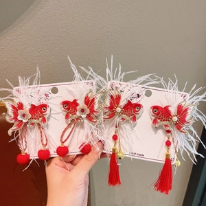Detail view of handmade New Year hair clips with red embroidery fish and soft feathers