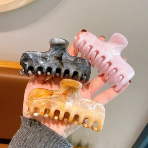 Detailed close-up of three large marble acrylic claw clips in black, pink, and amber colors